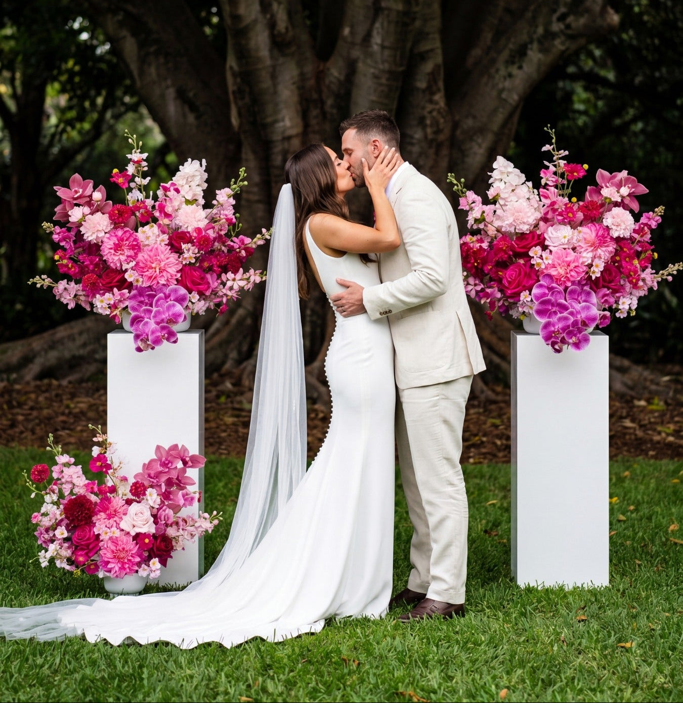 Couple kissing in a garden setting with floral arrangements on pedestals.